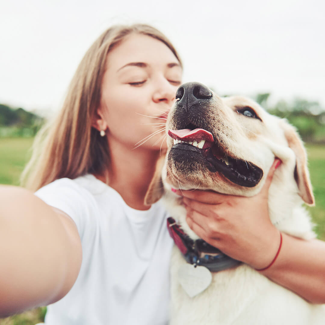 Woman taking a selfie while kissing a yellow Labrador
