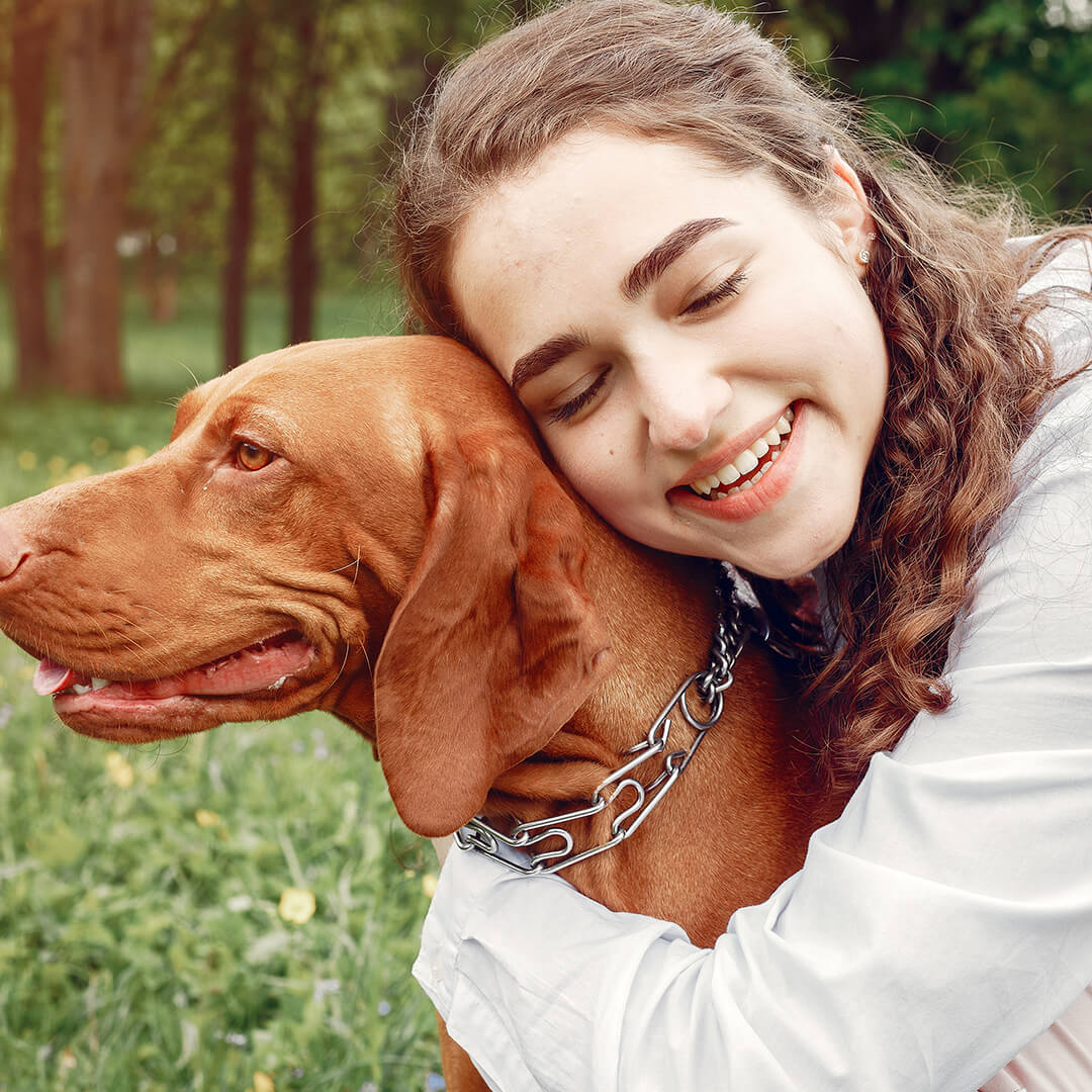 Smiling woman hugging a Vizsla dog in a park